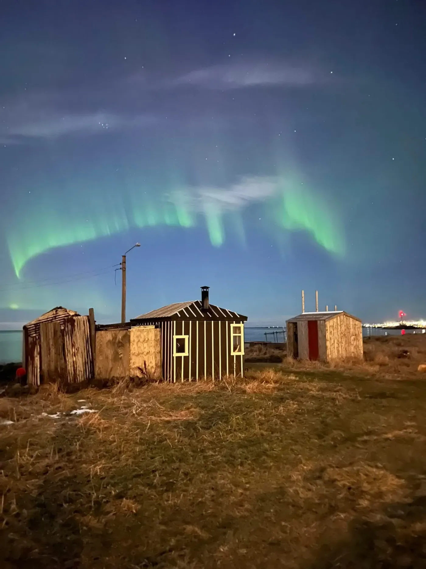 Small wooden seaside sauna huts under a green aurora