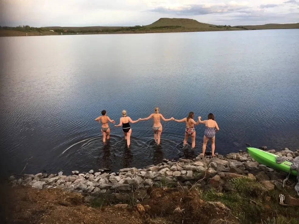 A group walking hand in hand into a lake at dusk
