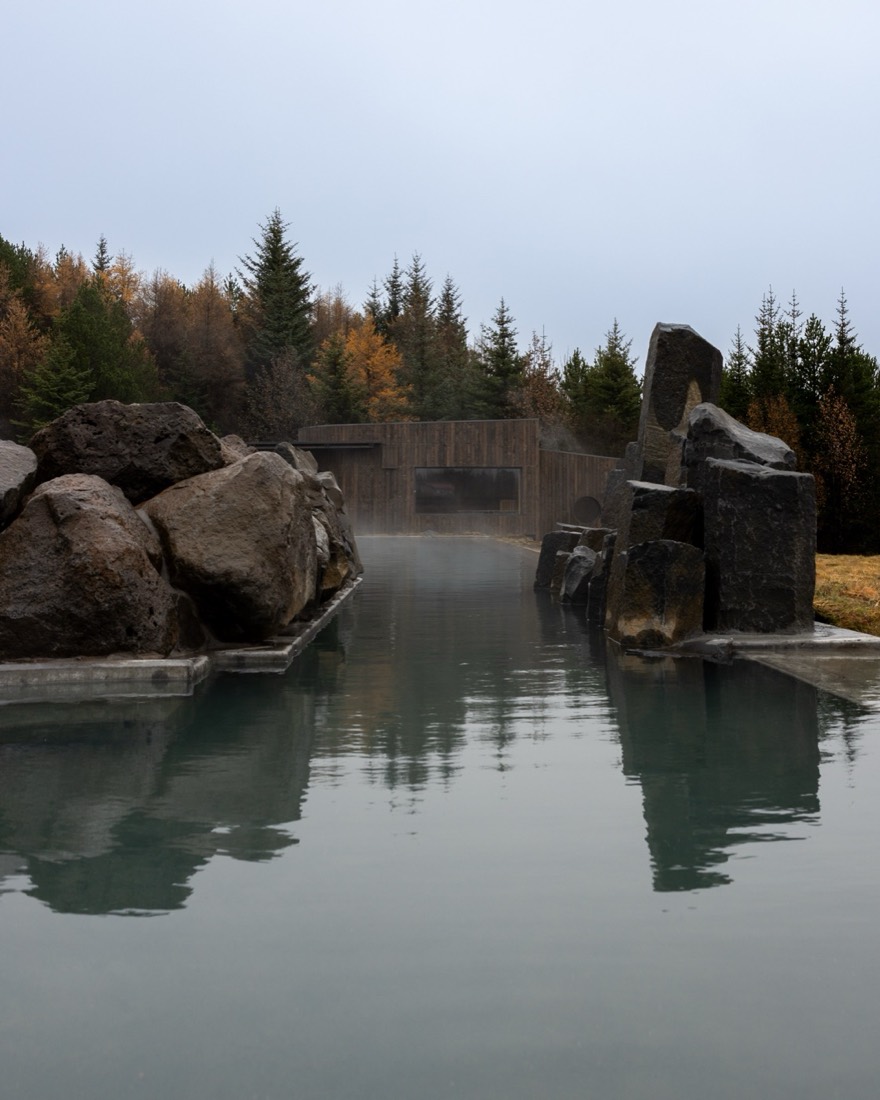 A stone-walled geothermal pool ringed by trees